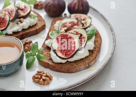 Sandwichs aux figues, fromage à la crème, basilic et miel sur assiette sur fond de bois, gros plan Banque D'Images