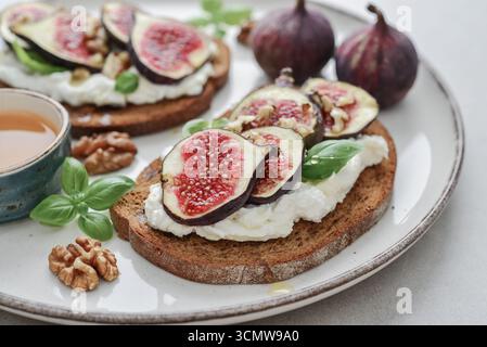 Sandwichs aux figues, fromage à la crème, basilic et miel sur assiette sur fond de bois, gros plan Banque D'Images