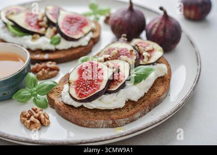 Sandwichs aux figues, fromage à la crème, basilic et miel sur assiette sur fond de bois, gros plan Banque D'Images