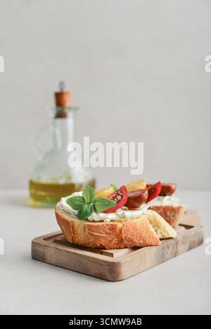 Sandwichs bruschetta avec tomates, fromage à la crème, huile d'olive et basilic sur une assiette sur fond clair. Antipasti italiens traditionnels. Banque D'Images