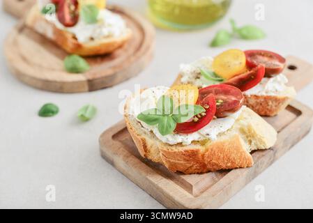 Sandwichs bruschetta avec tomates, fromage à la crème, huile d'olive et basilic sur une assiette sur fond clair. Antipasti italiens traditionnels. Banque D'Images