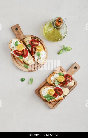 Sandwichs bruschetta avec tomates, fromage à la crème, huile d'olive et basilic sur une planche à découper en bois sur fond clair, vue de dessus. italien traditionnel an Banque D'Images