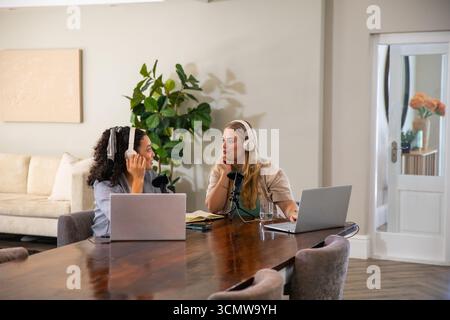 Diverses amies enregistrant des podcasts dans le salon à l'aide d'écouteurs, microphones, ordinateurs portables Banque D'Images