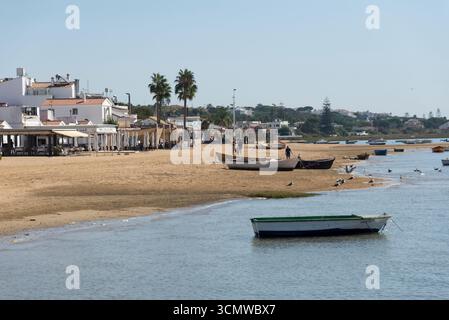 Barcas en el Agua y en la orilla en El Rompido con casas y restaurantes al borde la playa, reflejando la vida costera tradicional y turística. Banque D'Images