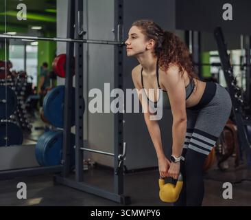 Athlétique jeune femme en forme faisant de l'exercice avec kettlebell dans le gymnase. Haltères, entraînement fonctionnel Banque D'Images