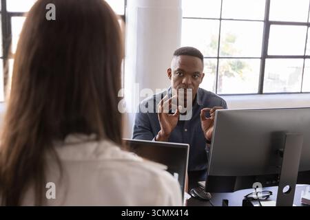 Divers collègues discutent des détails du projet au bureau avec deux moniteurs, clavier et téléphone de bureau Banque D'Images