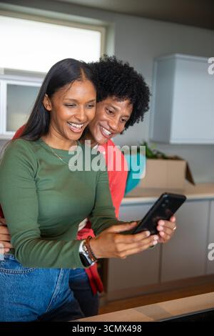 Couple diversifié déballer la serviette et la plante de la boîte, tenant le smartphone au comptoir de cuisine à la maison Banque D'Images