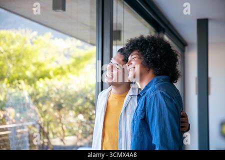Divers partenaires masculins embrassant et regardant à travers la fenêtre du sol au plafond dans le salon, espace de copie Banque D'Images