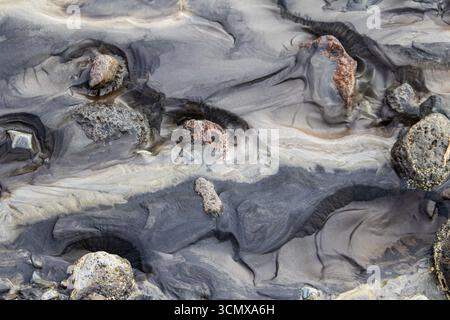 Vue abstraite de roches colorées noyées dans le sable gris du lit de la rivière à Maelifellssandur, Islande Banque D'Images