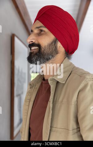 Homme indien debout dans le couloir portant un turban rouge et une veste beige, observant des œuvres encadrées Banque D'Images