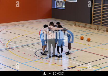 Équipe masculine de basket-ball diversifiée se blottissant sous le cerceau sur un terrain poli avec des ballons de basket-ball orange à proximité Banque D'Images