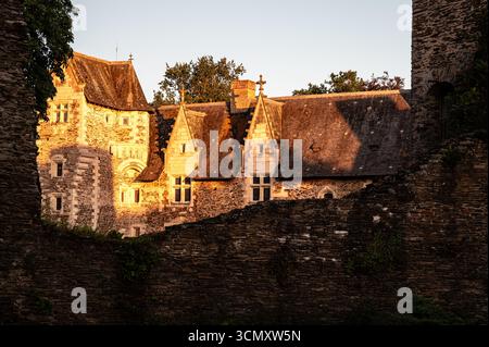 La lumière de l'heure d'or illumine les bâtiments de la cour du Château du Plessis-Macé, vus à travers une brèche dans le mur défensif extérieur. Banque D'Images
