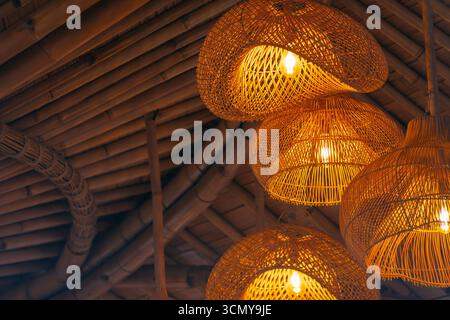 Lampes suspendues en rotin tissé brillantes d'une lumière chaude sous un intérieur de plafond en bambou. Banque D'Images