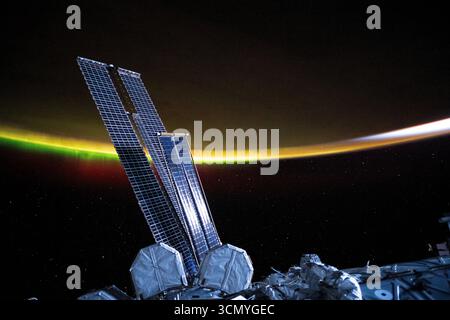Panneaux solaires de l’ISS avec l’atmosphère lumineuse de la Terre en arrière-plan. Banque D'Images