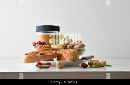 Détail des tranches de pain avec du beurre d'arachide étalé sur une assiette avec des bols d'arachides avec et sans coquille et un pot en verre plein de beurre d'arachide sur un Banque D'Images