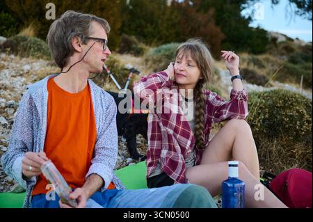 Deux amis assis de façon décontractée dans un cadre extérieur naturel, appréciant la compagnie et la conversation. Les tons terreux et la verdure donnent une ambiance sereine, accentuation Banque D'Images