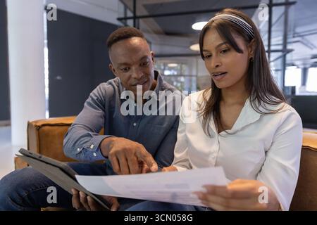 Divers collègues examinant l'impression tout en utilisant la tablette sur le canapé en cuir Havane dans le salon de bureau. Collaboration, professionnalisme, moderne, espace de travail, comm Banque D'Images