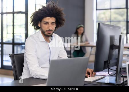 Divers collègues travaillant dans un bureau ouvert à l'aide d'un clavier de moniteur de bureau d'ordinateur portable et de papiers. Collaboration, moderne, espace de travail, productivité, équipe, Banque D'Images