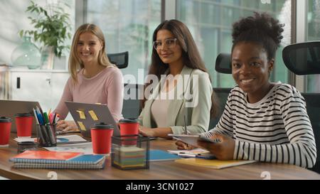 Trois femmes d'affaires informelles multiraciales travaillant dans le bureau des femmes d'affaires occasionnelles de diversité travaillent avec des ordinateurs portables écrivant des notes souriantes regardant Banque D'Images