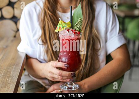 Femme tenant un cocktail d'été. Boisson rouge rafraîchissante froide avec de la glace et des fruits. Mode de vie sain des boissons en gros plan. Rafraîchissement le jour ensoleillé. Banque D'Images