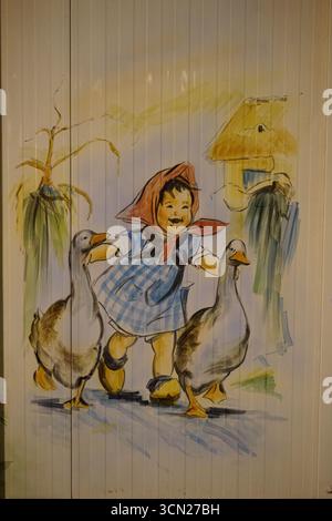 Fille ludique dans Red Hood marche avec des oies dans une scène rurale lumineuse avec des animaux ludiques. Bonifacio, Corse, France Banque D'Images