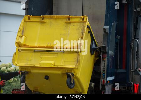 Grand conteneur de recyclage jaune vidé dans un camion à ordures pendant la collecte des déchets. Concept de recyclage, gestion des déchets, assainissement et ur Banque D'Images