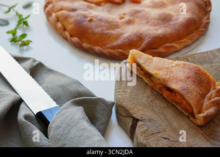 Empanada gallega placé sur une planche à découper en bois un dessus d'une table blanche Banque D'Images