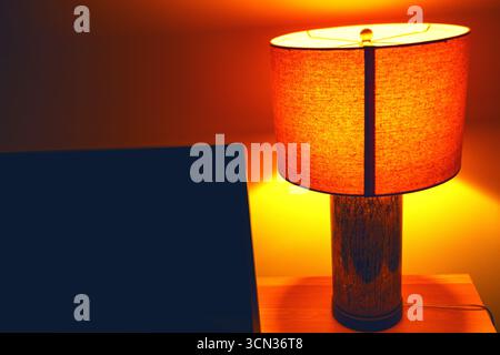 Ambiance accueillante avec lampe de table brillante avec abat-jour orange projetant la lumière ambiante dans la pièce. Création de profondeur et atmosphère chaleureuse. Ambiance chaleureuse Banque D'Images