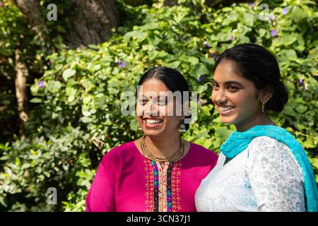 Mère indienne et fille souriant ensemble dans le jardin, portant magenta kurta et turquoise dupatta Banque D'Images