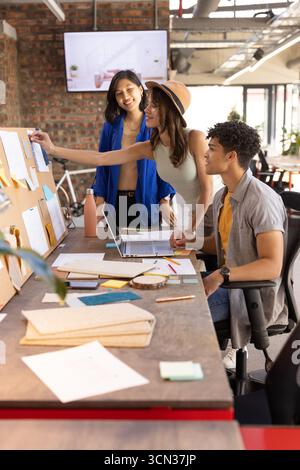 Divers collègues collaborant à table dans le bureau avec ordinateur portable, tableau de liège, notes autocollantes Banque D'Images