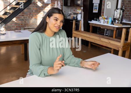 Femme assise à la table rectangulaire blanche dans le bureau avec ordinateur portable fermé sur la table d'appoint Banque D'Images