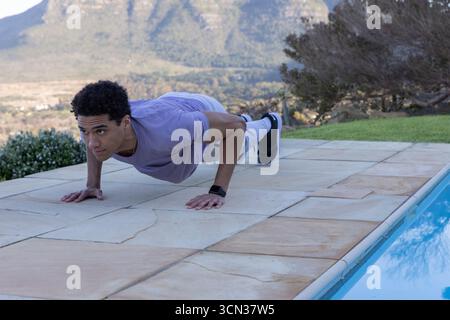 Homme afro-américain effectuant des pompes sur la terrasse à côté de la piscine dans les chaussures de course fitness tracker Banque D'Images