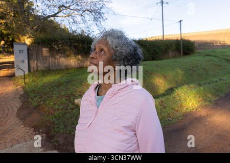 Femme afro-américaine senior debout sur l'allée près de la porte montrant le numéro de maison 27 Banque D'Images