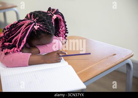Fille afro-américaine appuyée sur le bureau de l'école avec un crayon violet sur le cahier, espace de copie Banque D'Images