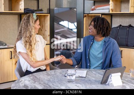Divers collègues serrant la main tout en étant assis à la table de conférence dans le bureau avec tablette Banque D'Images