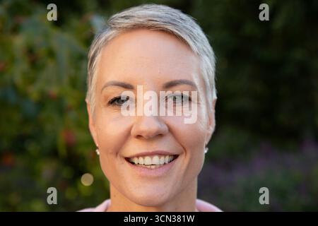 Femme senior souriant à la caméra dans le portrait de cour mettant en vedette des boucles d'oreilles de perles et le haut Banque D'Images