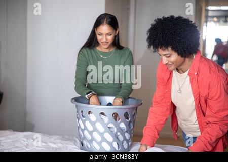 Divers couples triant et pliant le linge dans la chambre à coucher à la maison avec panier à linge Banque D'Images