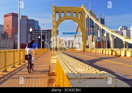 Un jeune homme adulte fait du vélo pour travailler sur le pont Roberto Clemente à Pittsburgh, en Pennsylvanie Banque D'Images