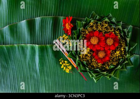 Krathong décore avec des fleurs rouges et jaunes qui ont flou le focus de 3 bâtons d'encens et bougie mis sur la feuille de banane pour le festival Loy Krathong. Banque D'Images