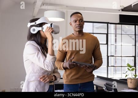 Divers collègues tenant la tablette et ajustant le casque vr au bureau près des fenêtres dans le bureau Banque D'Images