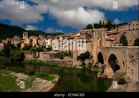 Les eaux vertes calmes de la rivière Fluvià reflètent les toits de tuiles rouges et les murs de gravats de pierre de Besalú, une ancienne ville catalane de Gérone, en Espagne. Les jupes de la rivière restent des murs défensifs après avoir coulé sous les arcs arrondis du Viejo reconstruit du 11ème siècle ou du Vieux Pont, qui se termine par une passerelle permettant l'accès à la vieille ville bien préservée. Banque D'Images