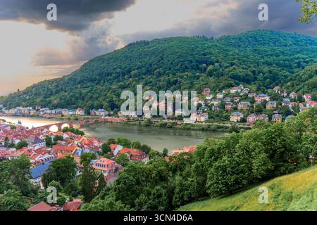 Vue panoramique sur la ville historique de Heidelberg avec la rivière Neckar, les maisons à flanc de colline et la verdure luxuriante sous un ciel spectaculaire au coucher du soleil. Banque D'Images