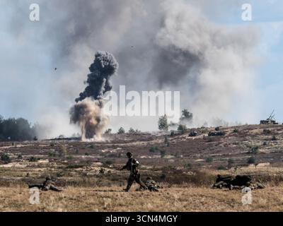 Explosions vues alors que des soldats d'infanterie polonais des Forces de défense territoriale s'entraînent à tirer à vue sous couvert lors de la journée médiatique Iron Defender 25. L’exercice Iron Defender 25 est l’événement d’entraînement le plus important et le plus important planifié par et pour les forces armées polonaises. Il s'agit d'une série d'exercices défensifs menés sur terre, dans les airs et sur l'eau par les forces terrestres, aériennes, navales, spéciales et territoriales de défense. Trente mille soldats et 600 pièces d'équipement des forces armées polonaises et des alliés de l'OTAN y participent. Banque D'Images