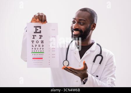 Portrait d'un médecin afro-américain souriant qui montre un test d'examen des yeux. Banque D'Images