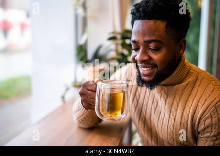Gros plan portrait du jeune homme noir qui est assis au bar et buvant du thé. Banque D'Images