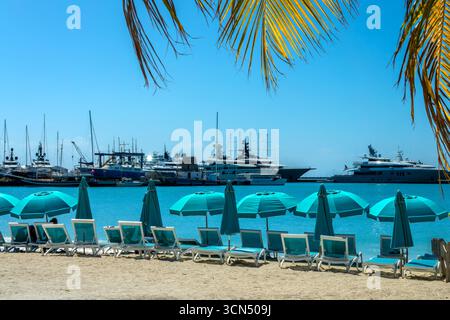 Chaises et parasols sur la plage de la Grande Baie avec des bateaux dans la marina de Philipsburg, paysage caribéen, île de St Maarten (St Martin), Antilles néerlandaises Banque D'Images
