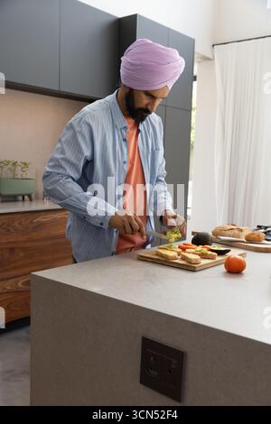 Homme indien d'âge moyen tranchant des légumes sur l'îlot de cuisine en pierre à l'aide d'une planche à découper, tomates Banque D'Images