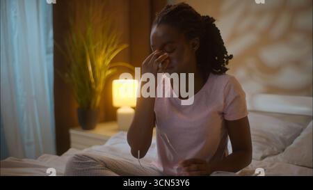 Épuisé afro-américain femme d'affaires femme client femme d'affaires étudiante travail devoirs ordinateur portable sur le lit décollant lunettes frottant pont Banque D'Images