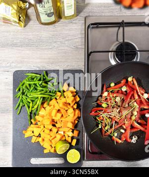 Vue de dessus d'un comptoir de cuisinière de cuisine avec des légumes tranchés, y compris du poivron rouge, des haricots verts et de la courge à côté d'une poêle de cuisson sur une cuisinière Banque D'Images