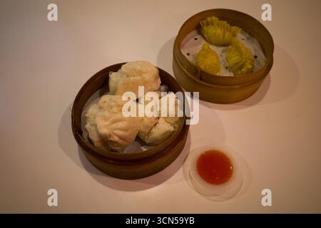 Bakpao, petits pains chinois cuits à la vapeur remplis de chocolat sur panier en bambou et sauce Chili. Banque D'Images